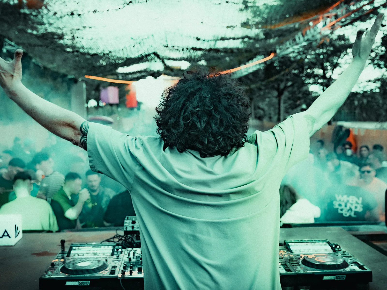 DJ con los brazos en alto frente al público, entre humo verde